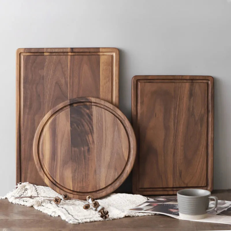 Solid black walnut wood cutting board with juice groove and side handle, shown in round and rectangular sizes.