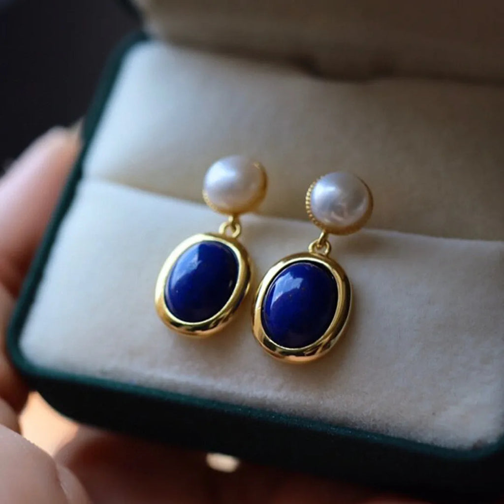 A pair of simple silver drop earrings with blue lapis lazuli pearls and auspicious pattern detailing.
