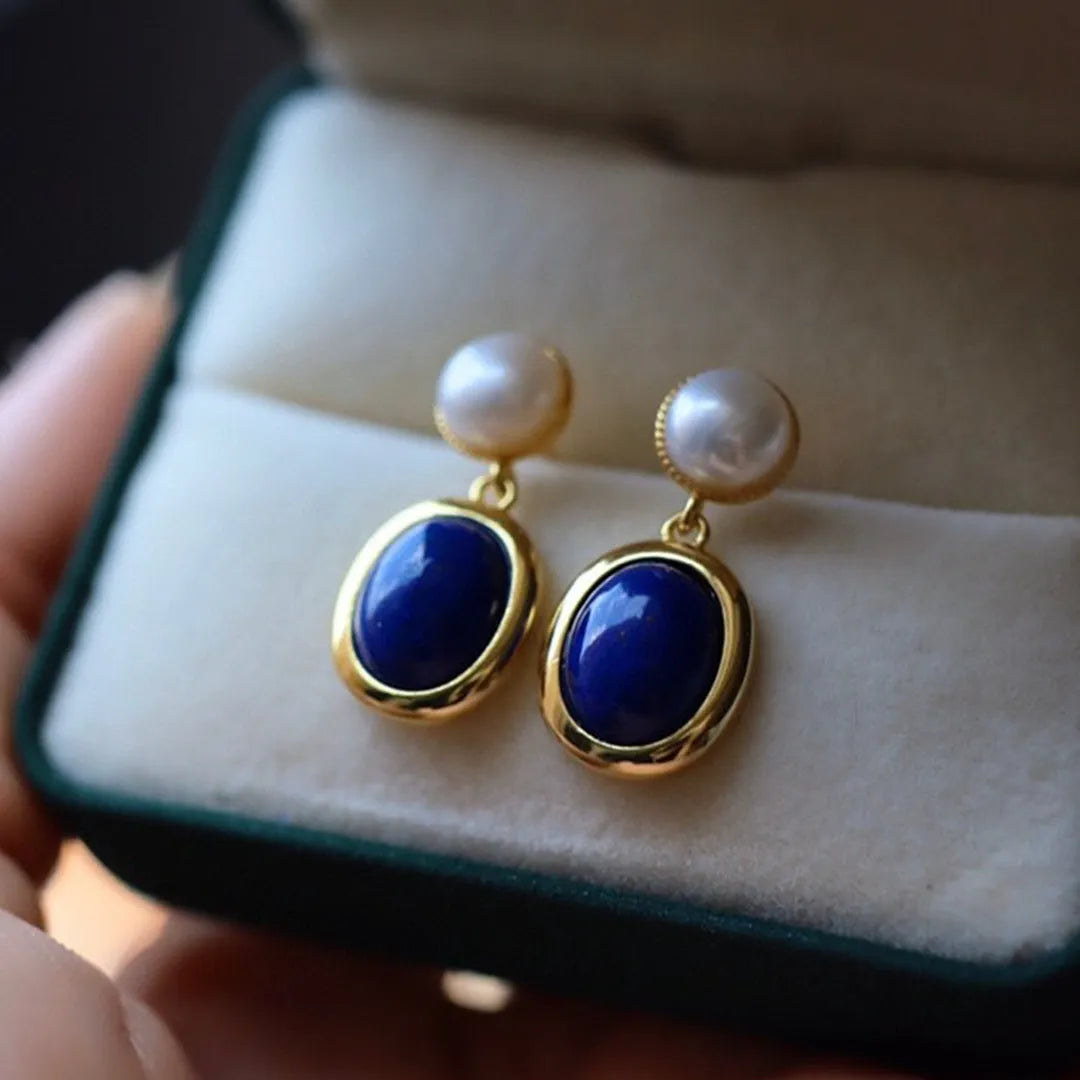 A pair of simple silver drop earrings with blue lapis lazuli pearls and auspicious pattern detailing.
