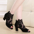Black lace gladiator sandals with a square high heel and zip closure on a woman's foot.