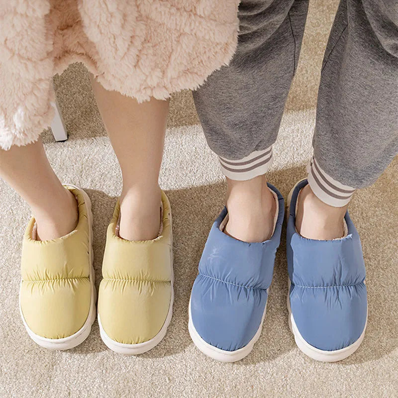 A pair of blue down cotton slippers with a thick rubber sole and artificial leather upper on a wooden floor.
