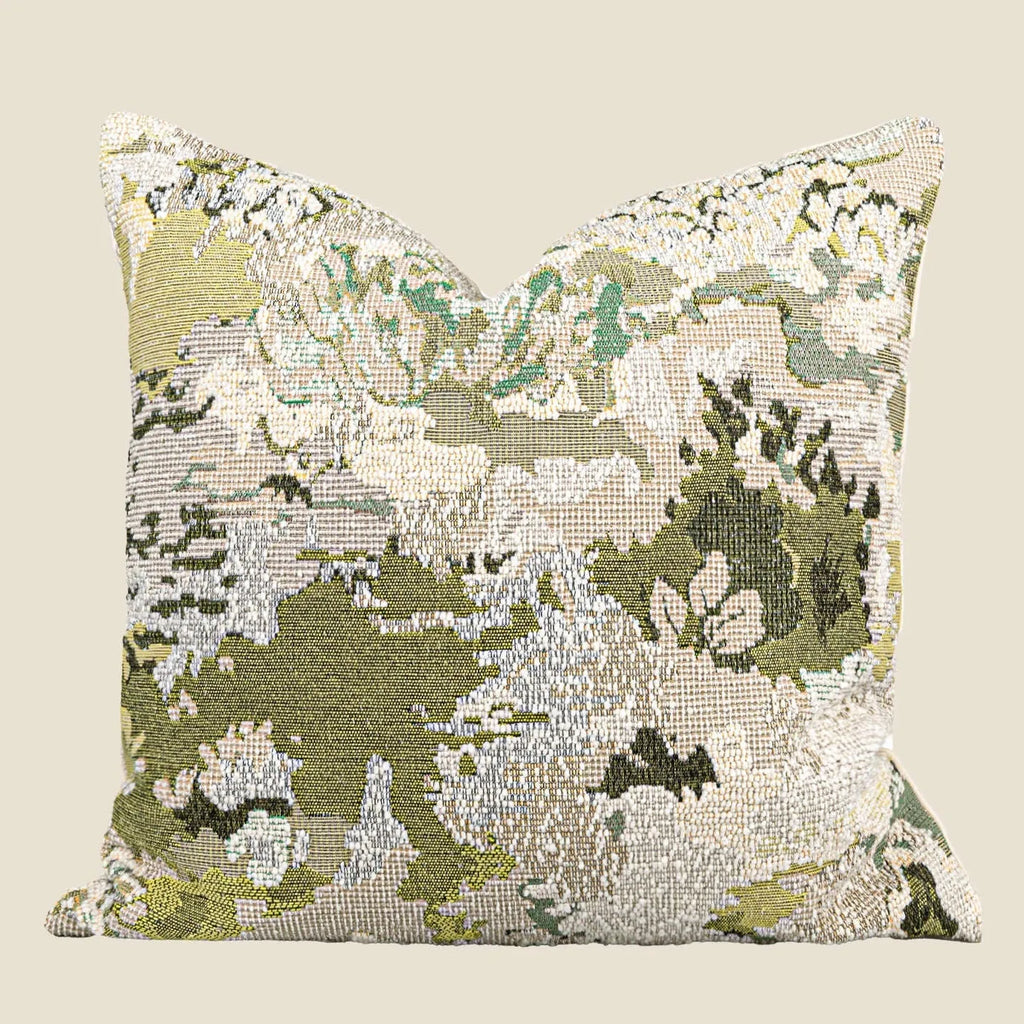 Green square pillow with abstract botanical plant and flower pattern on a sofa.