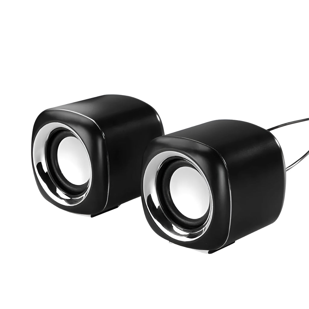 Pair of small black cube-shaped wired computer speakers with a 3.5mm plug on a desk