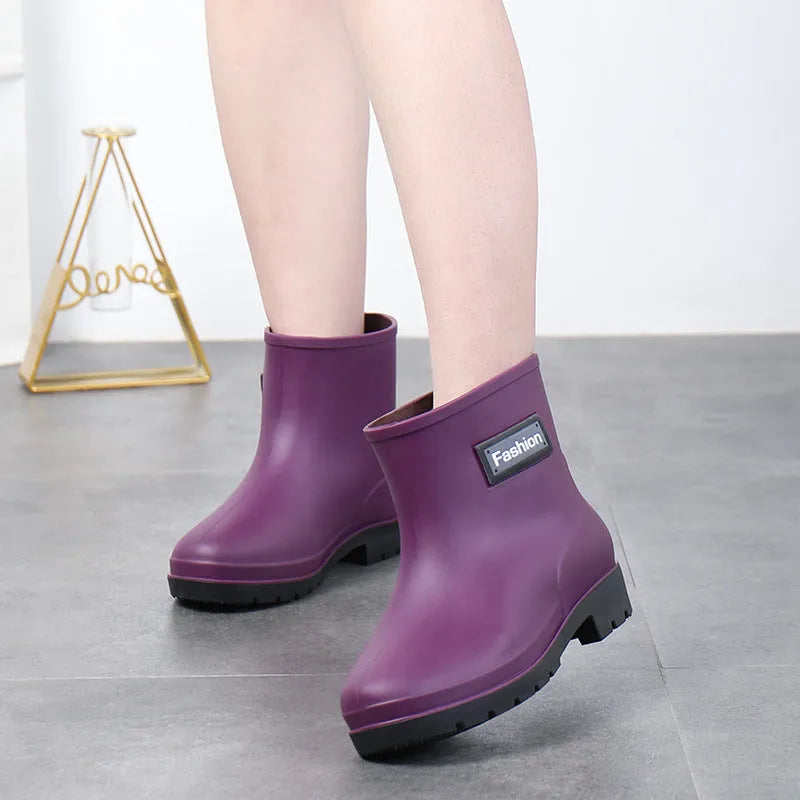 Women's black PVC mid-calf rain boots with a low heel on a wet surface.