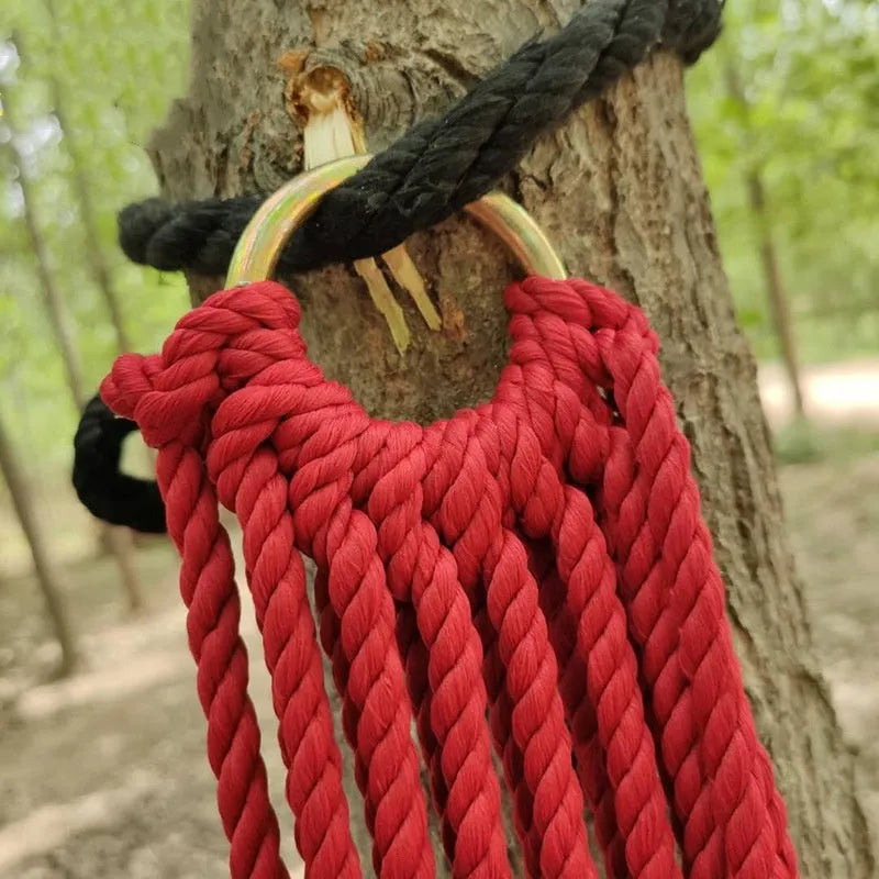 Outdoor nylon rope mesh hammock hung between two trees showing its open weave and supplied tying hardware.