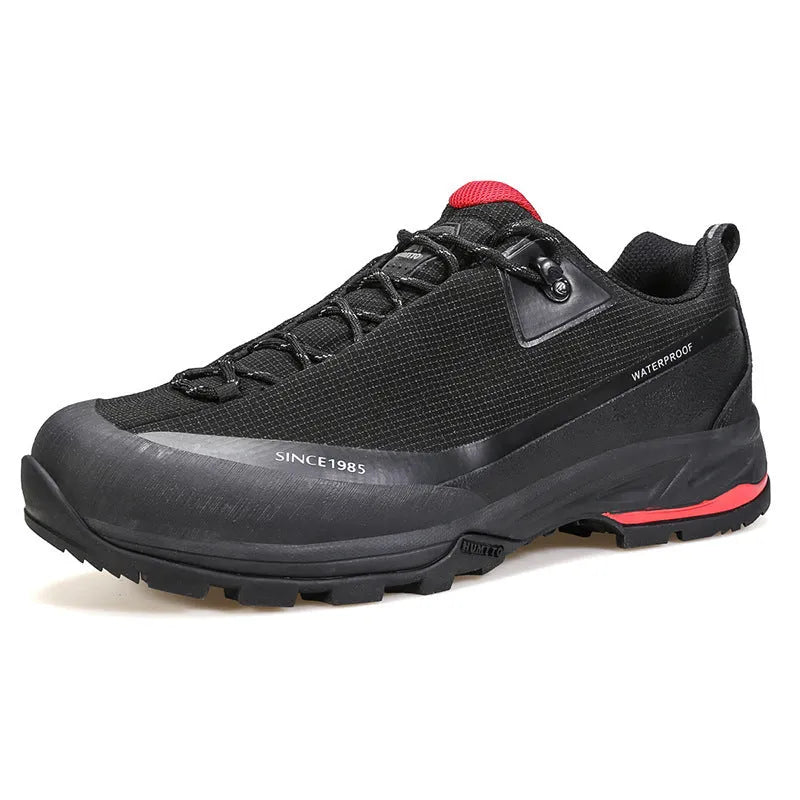 Men's low-top hiking boots in dark grey with round toe and front lace-up design on a rocky trail.