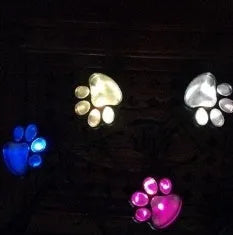 Four black animal paw print solar garden lights with stakes and one central solar panel