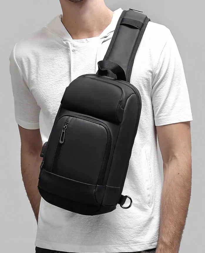 Black PVC outdoor shoulder bag with a square shape, showing the air cushion strap and front pocket.