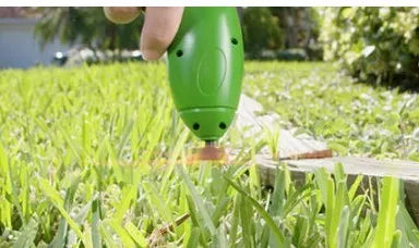 Cordless handheld lawn trimmer with extension pole and protective shield on green grass