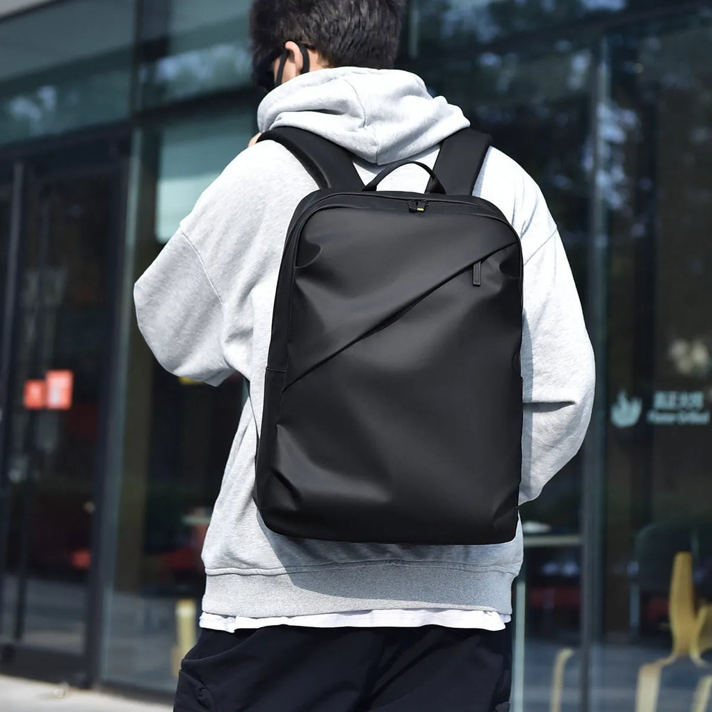 Men's waterproof PU backpack in black with simple sewing thread design and separate computer compartment.