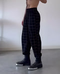 Man wearing grey plaid trousers with a contrasting darker apron panel across the front