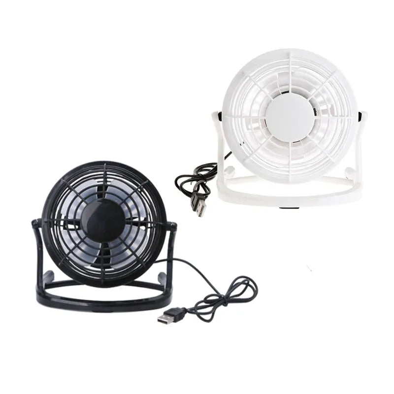 Mini black USB desk fan on a table next to a laptop, showing adjustable tilt angle.