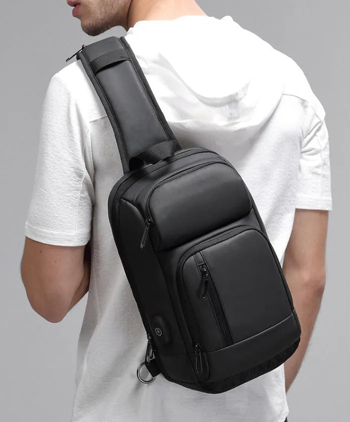 Black PVC outdoor shoulder bag with a square shape, showing the air cushion strap and front pocket.