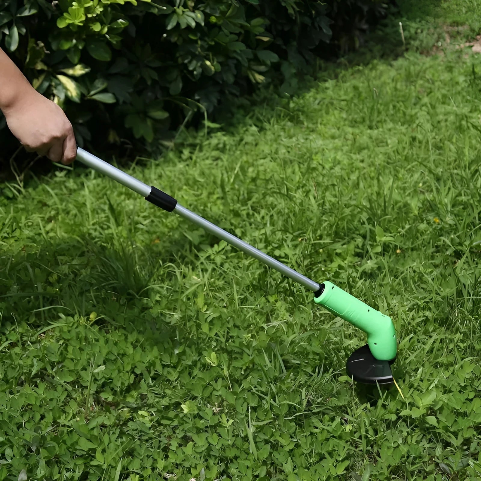 Cordless handheld lawn trimmer with extension pole and protective shield on green grass