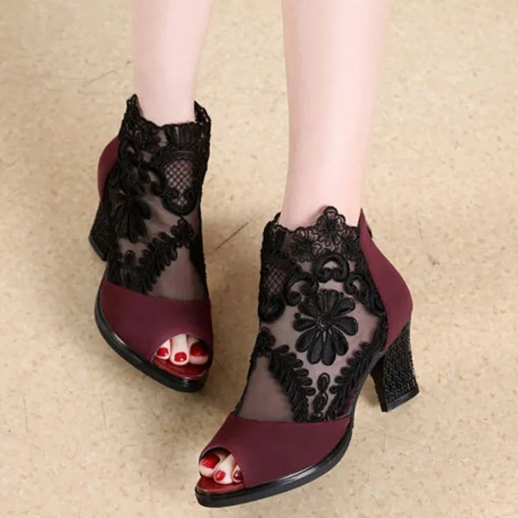 Black lace gladiator sandals with a square high heel and zip closure on a woman's foot.