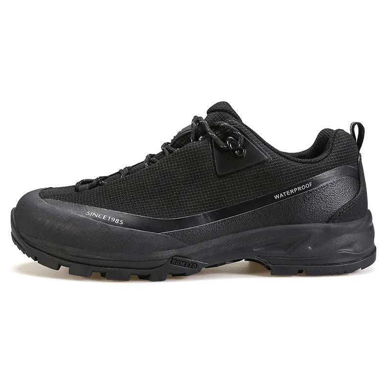 Men's low-top hiking boots in dark grey with round toe and front lace-up design on a rocky trail.