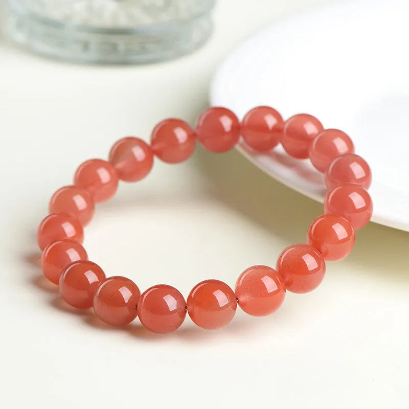 Natural cherry red agate bead bracelet on a wrist, showing polished stones and string construction.