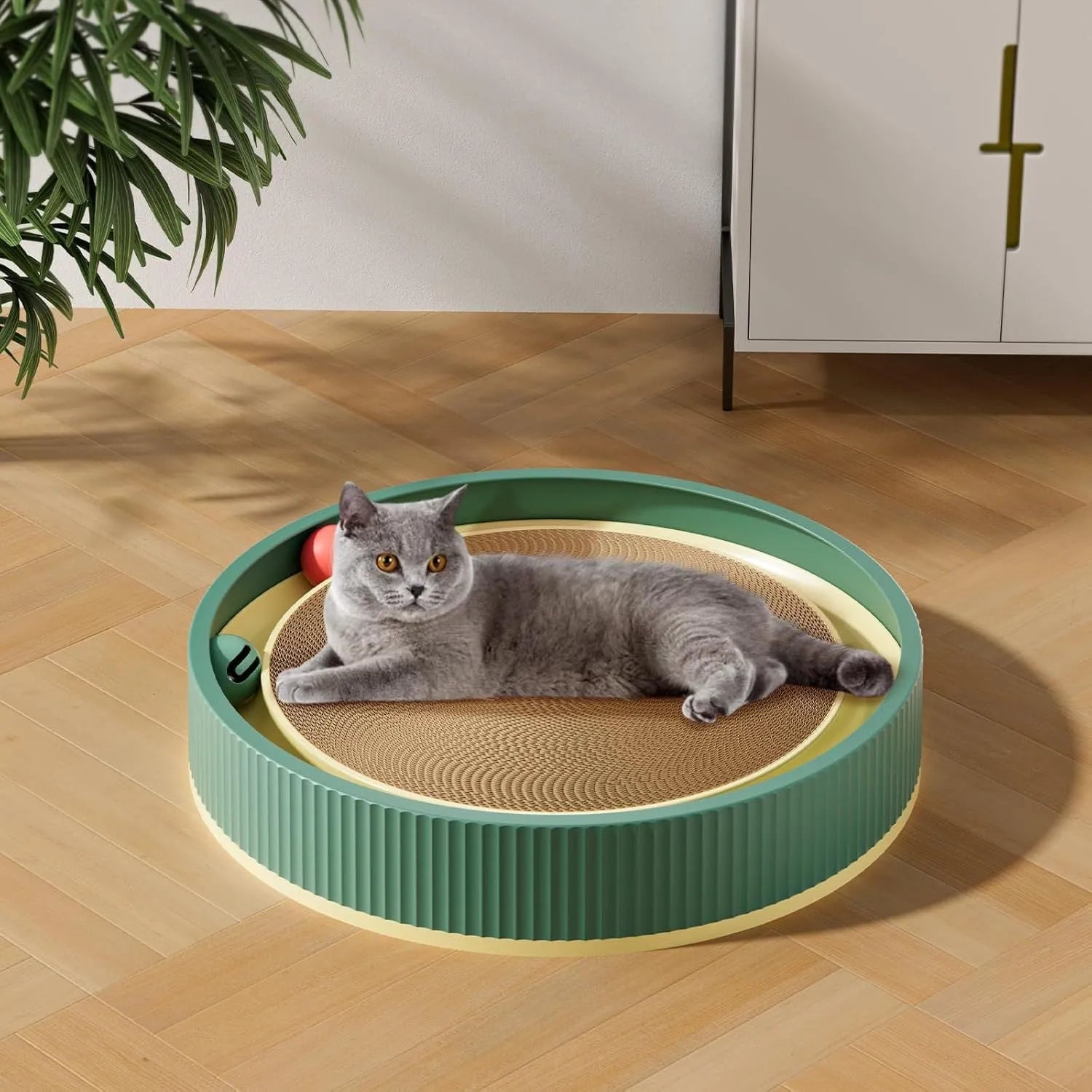 Large circular green cardboard cat scratching board with a central track containing two yellow balls and a spring-mounted plush ball.