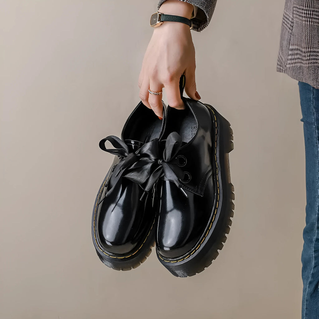 Women's black thick-soled leather-style lace-up shoes with ribbon and cross strap details on a white background.