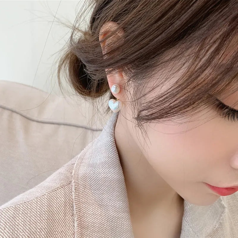 Close-up of women's heart-shaped alloy stud earrings with pearl-like appearance and electroplated finish.