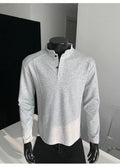 Man wearing a loose fit grey long sleeve sweater with an asymmetric design and a stand-up polo shirt collar.