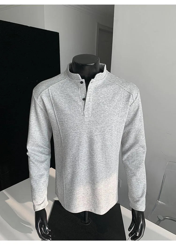 Man wearing a loose fit grey long sleeve sweater with an asymmetric design and a stand-up polo shirt collar.