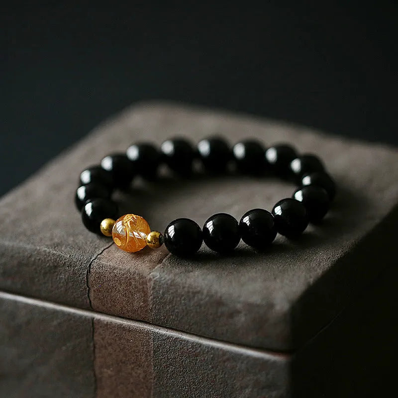 Unisex geometric beaded bracelet with obsidian, white crystal, and a gold dragon bead on a black background