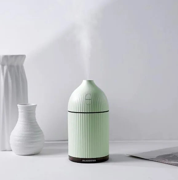 White square aromatherapy diffuser and humidifier with LED light on a wooden desk.
