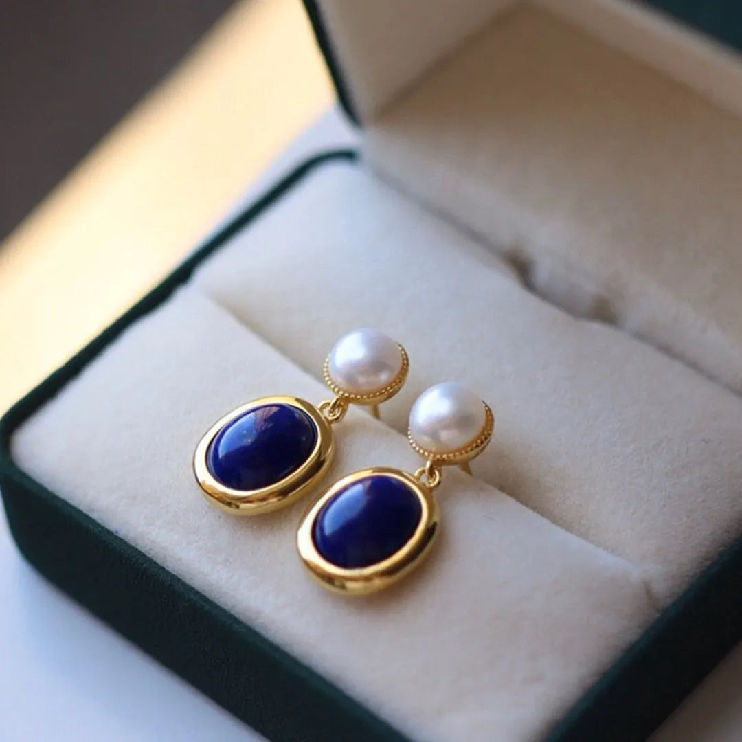A pair of simple silver drop earrings with blue lapis lazuli pearls and auspicious pattern detailing.