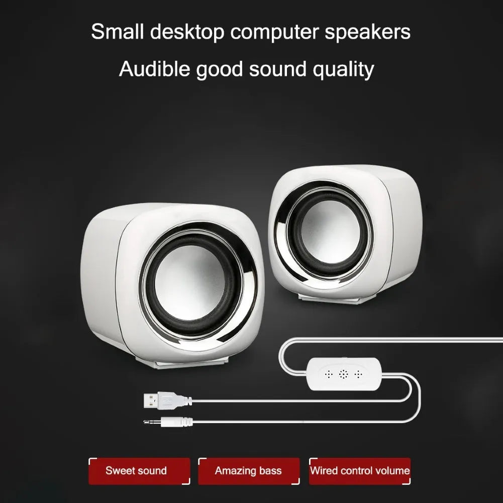 Pair of small black cube-shaped wired computer speakers with a 3.5mm plug on a desk