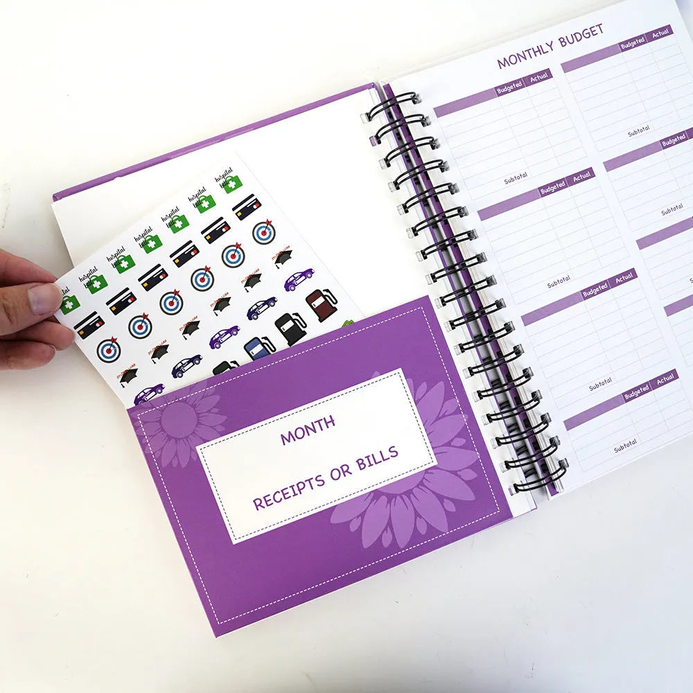 J12 purple coil-bound budget notebook with financial planning stickers and paper clips laid out.