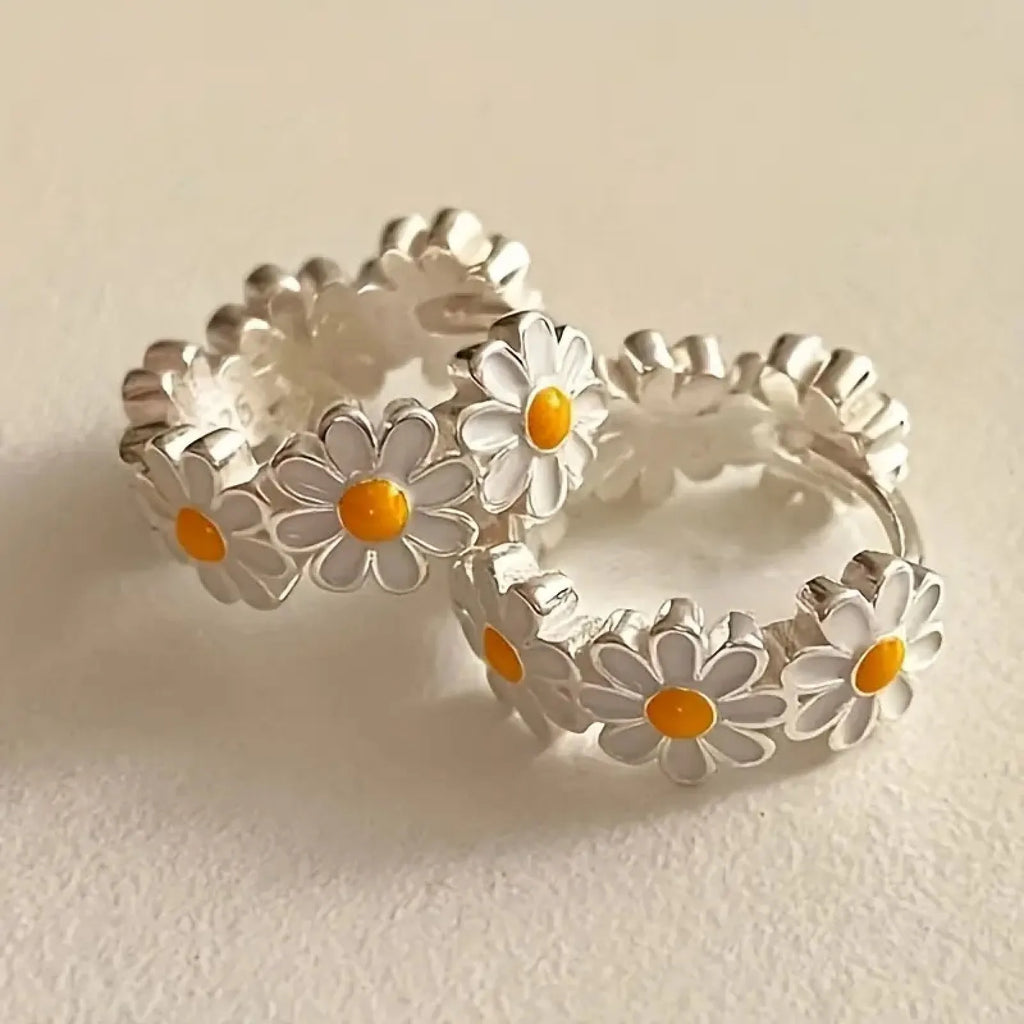 Close-up of white daisy flower ring earrings with gemstone centre on copper setting.