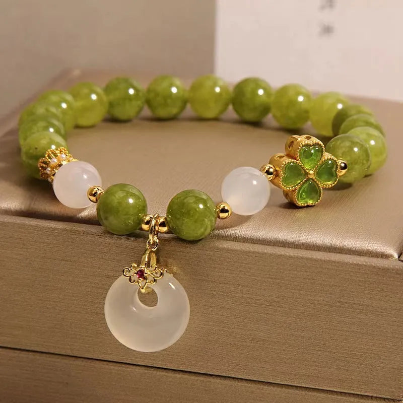 Women's green tourmaline bracelet with four-leaf clover charm and geometric drop pendant on a safety buckle.