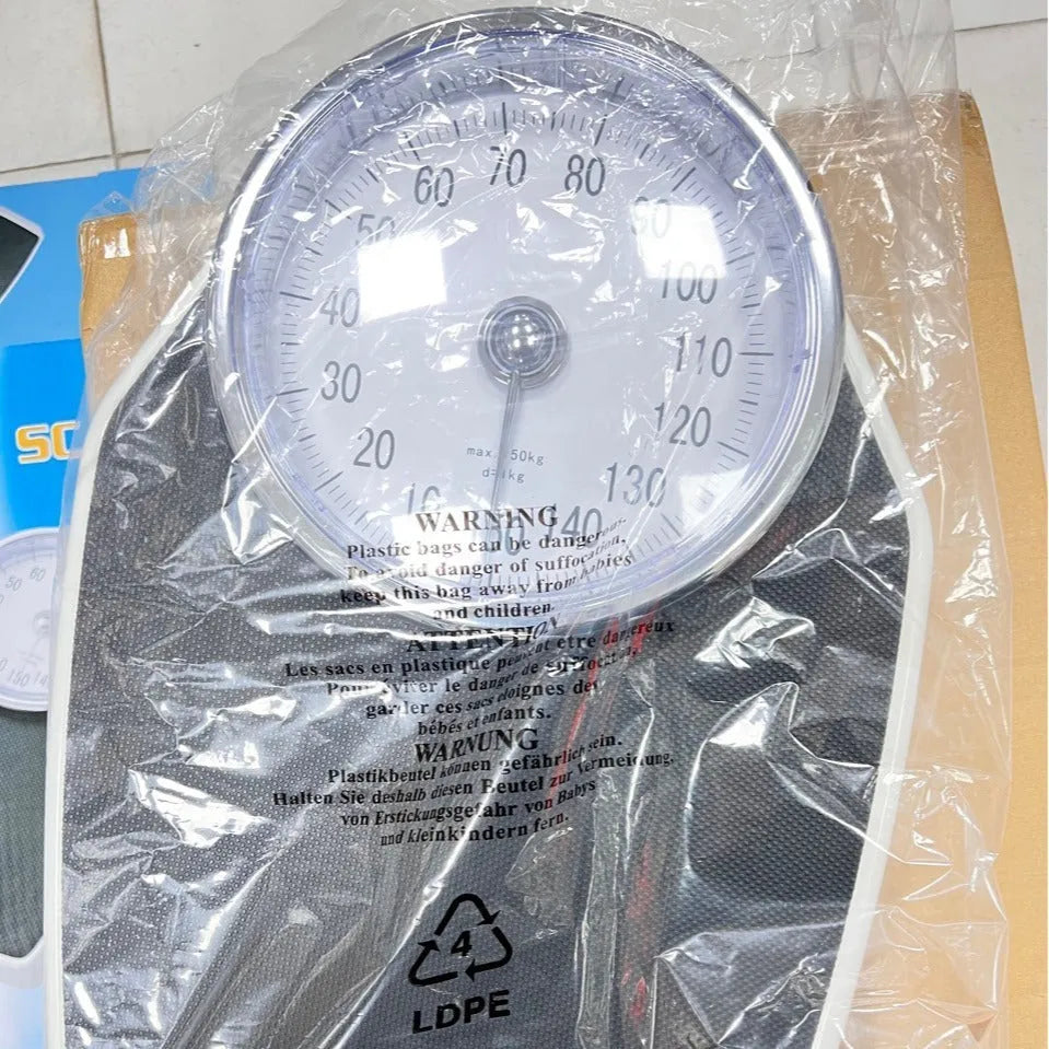 Black mechanical bathroom scale with large analogue dial showing weight pointer, placed on a floor.