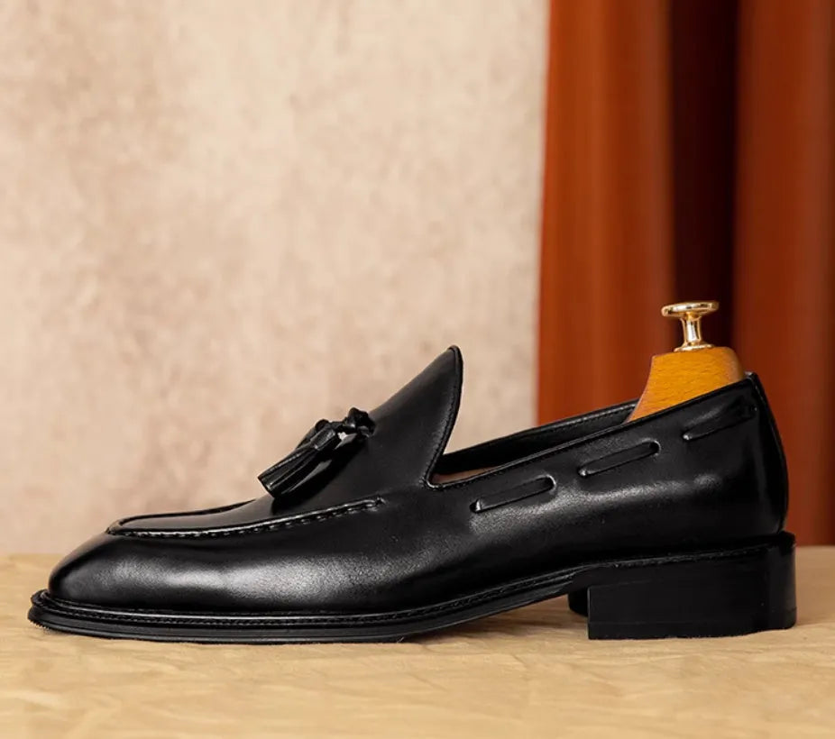 Men's black genuine leather slip-on loafers with fringed detailing and a rubber sole, shown from a side view.