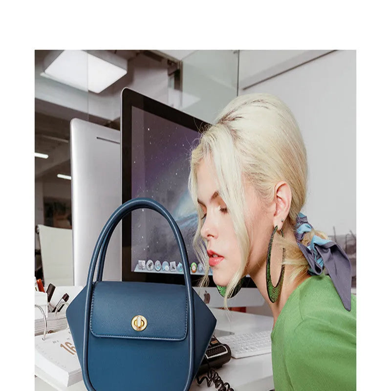 A wing-shaped cow leather tote bag with a buckle latch closure, shown in blue with a single cross-body strap.