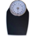 Black mechanical bathroom scale with large analogue dial showing weight pointer, placed on a floor.