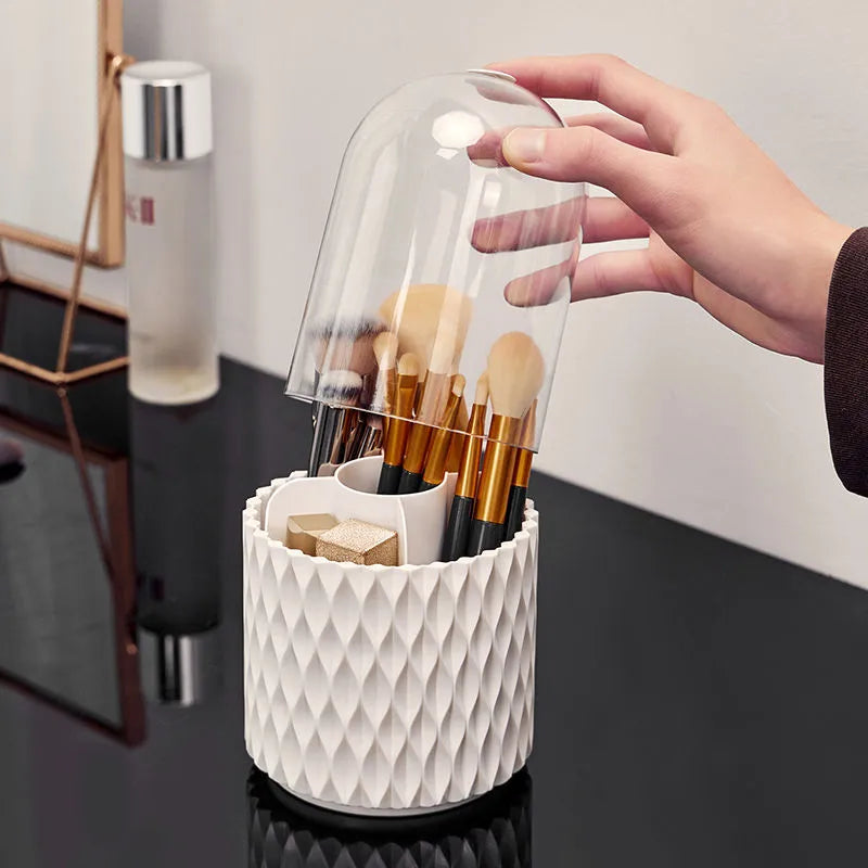 White acrylic rotating makeup brush holder with transparent body and a grey dust cover on a desk.