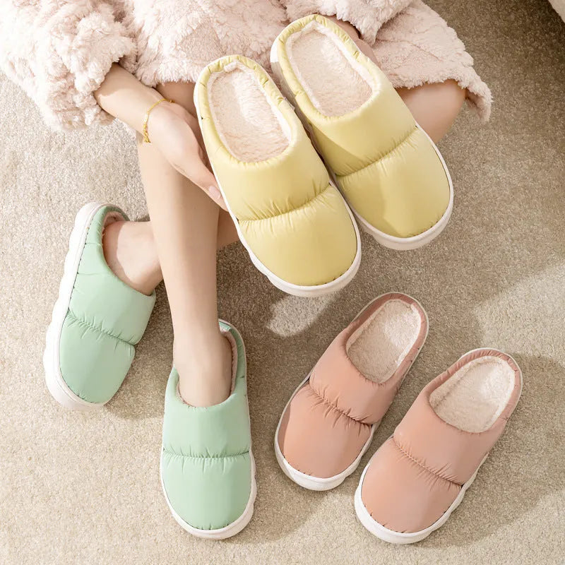 A pair of blue down cotton slippers with a thick rubber sole and artificial leather upper on a wooden floor.
