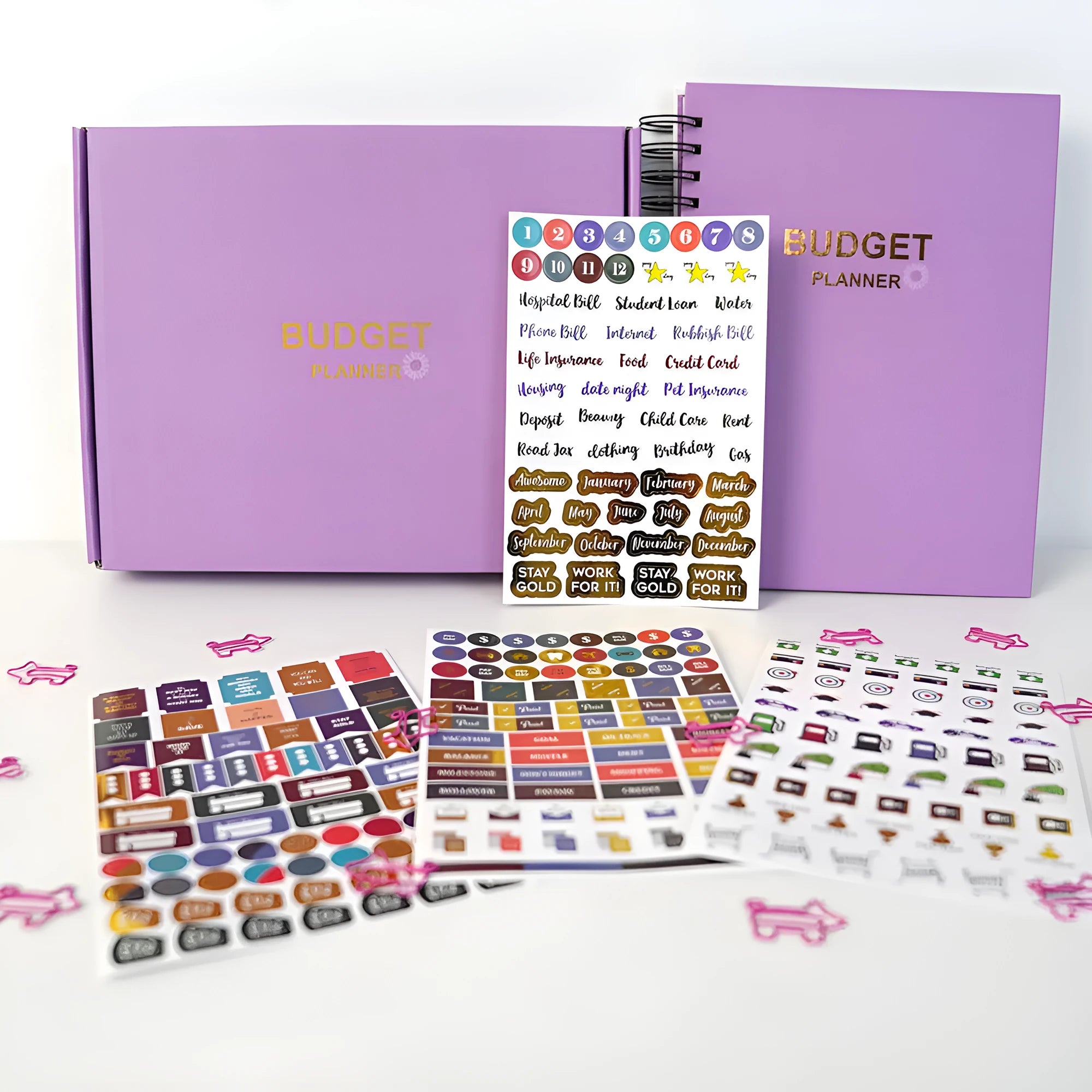 J12 purple coil-bound budget notebook with financial planning stickers and paper clips laid out.