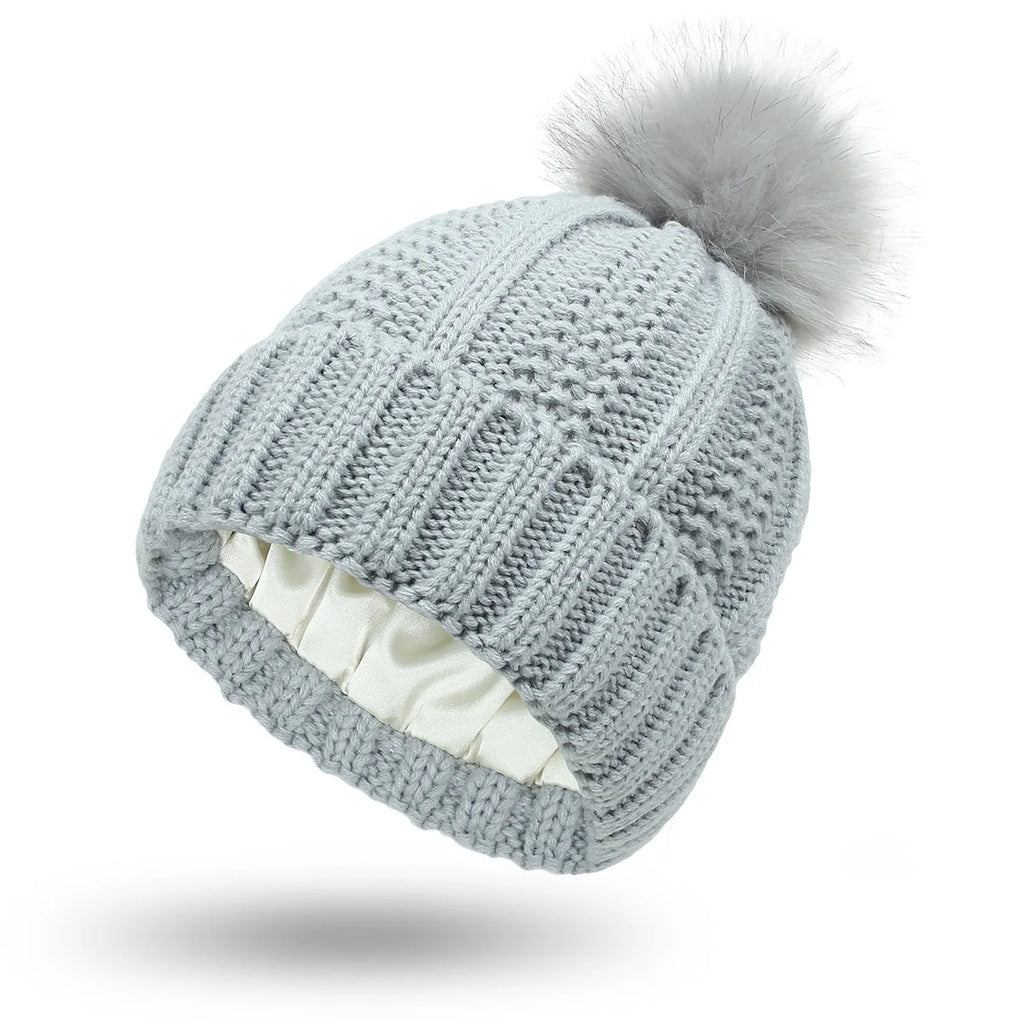 Women's black knit beanie with a faux fur pom pom and a visible satin lining inside the crown.