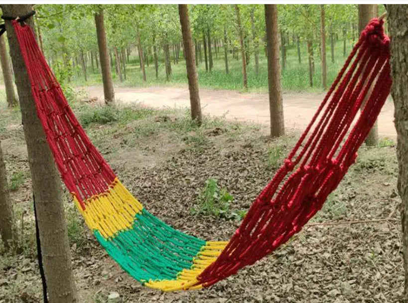 Outdoor nylon rope mesh hammock hung between two trees showing its open weave and supplied tying hardware.