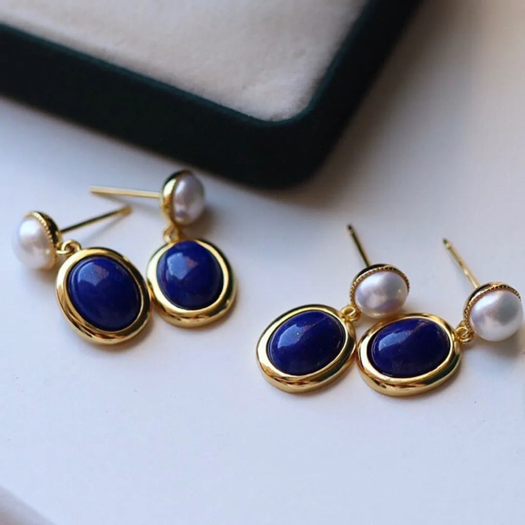A pair of simple silver drop earrings with blue lapis lazuli pearls and auspicious pattern detailing.