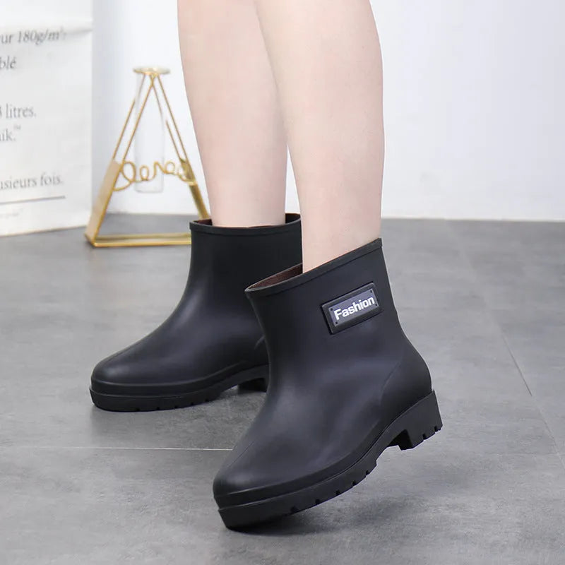 Women's black PVC mid-calf rain boots with a low heel on a wet surface.