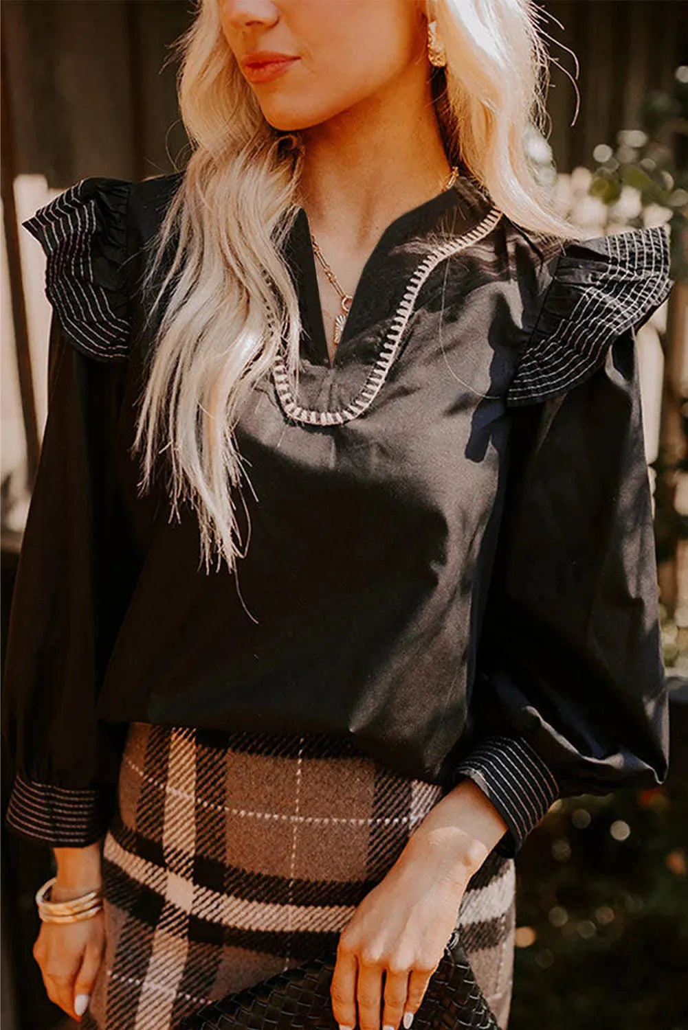 Black women's V-neck blouse with long ruffle sleeves and white contrast stitching.