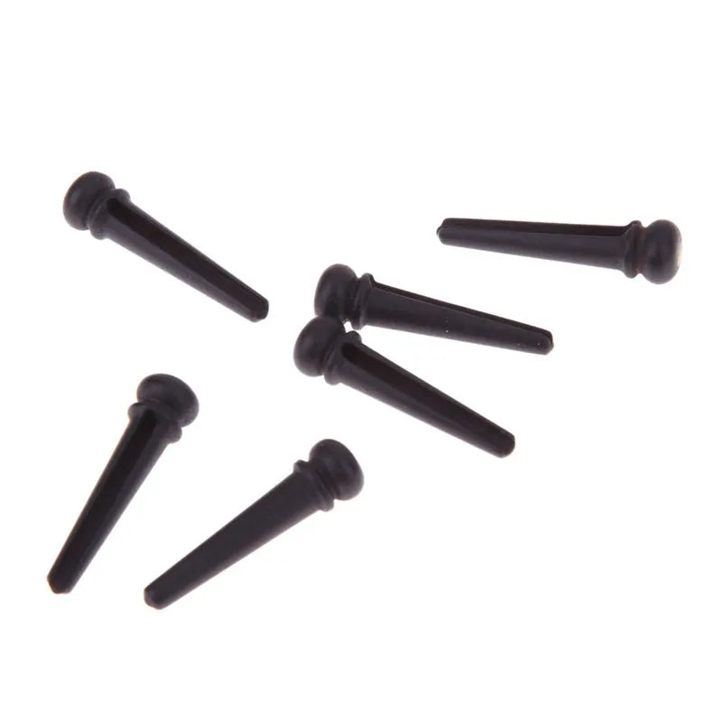 Six ebony guitar bridge pins with matt black finish on dark surface