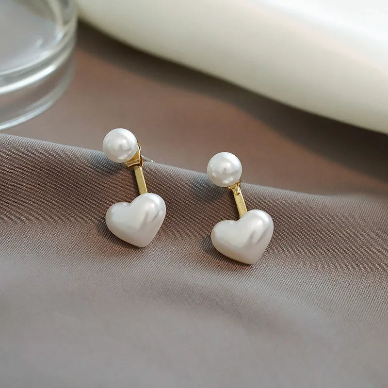 Close-up of women's heart-shaped alloy stud earrings with pearl-like appearance and electroplated finish.