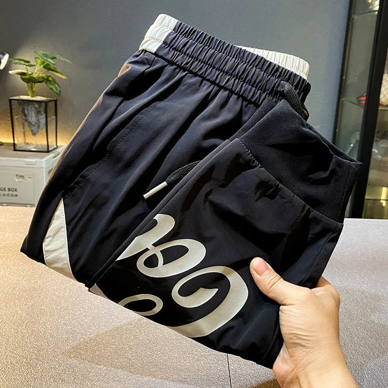 Men's solid black ultra-thin ice silk ankle-banded cropped casual trousers laid flat.