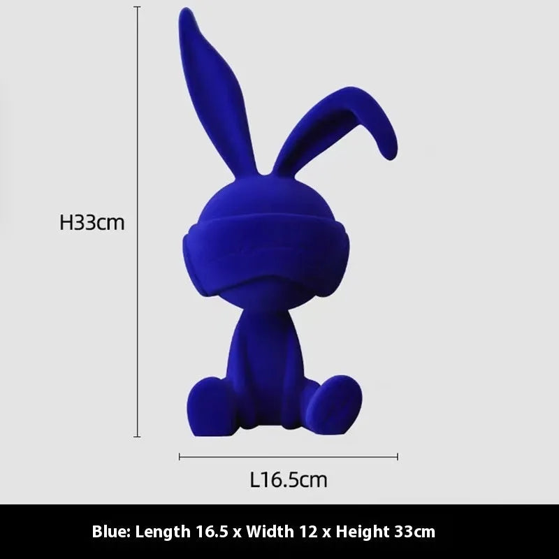 Suede blindfold rabbit resin ornament in green, blue, or red colours on a shelf.