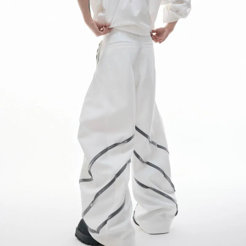 Men's black trousers with three-dimensional cut, metal striped rivet details and pleats on a white background.